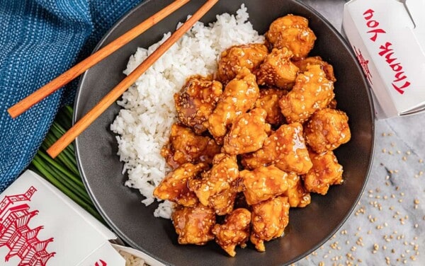 Overhead view of a bowl of white rice with takeout sesame chicken.
