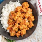 A black dinner bowl filled with white rice and takeout sesame chicken.