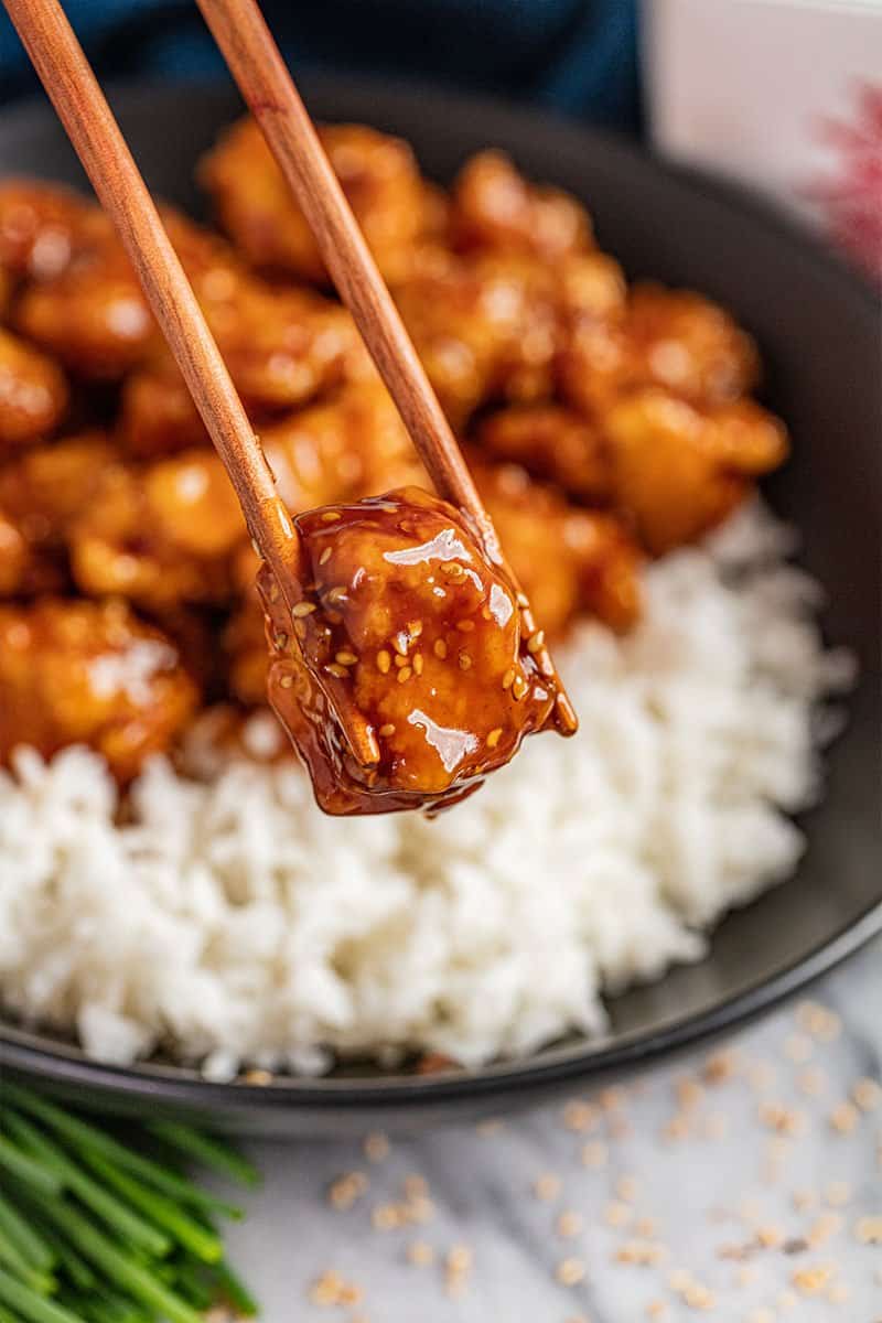 Chopsticks hold up a piece of crispy and sweet sesame chicken.