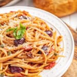 Pasta puttanesca on a white plate.