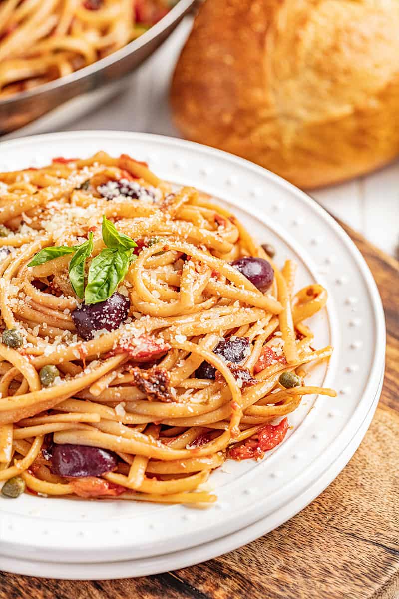 Pasta puttanesca on a white plate.