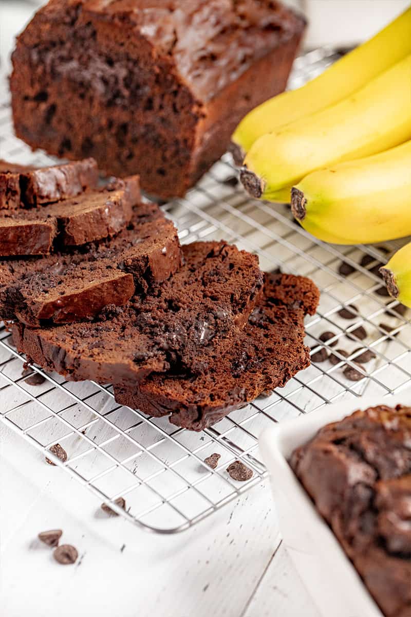 A loaf of chocolate banana bread cut into slices on a wire rack.