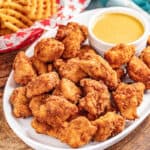 Copycat Chick Fil-A nuggets met dipsaus op een serveerschaal met wafelfrietjes ernaast.