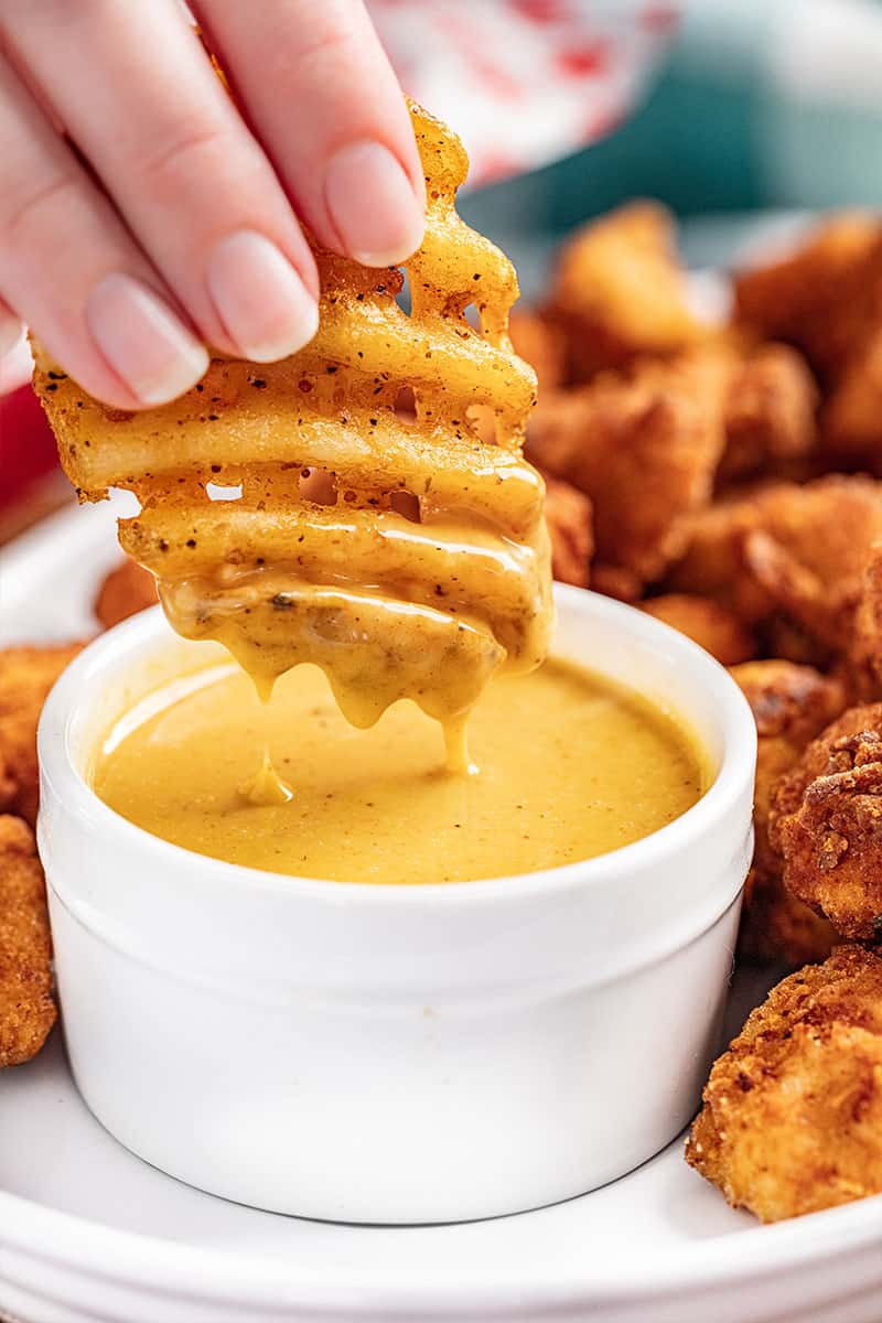 A hand dipping a waffle fry into copycat chick fil-a sauce.