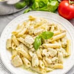 Chicken pesto pasta on a white plate with fresh basil.