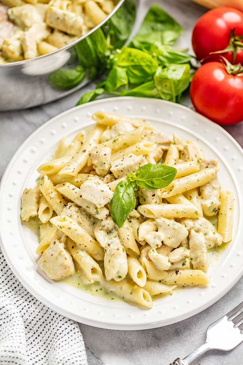 Chicken pesto pasta on a white dinner plate with fresh basil.