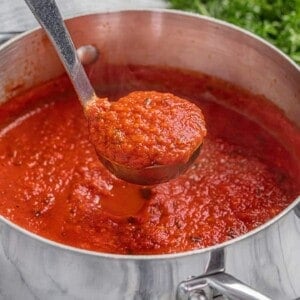 A ladle of spaghetti sauce being held over a stockpot.