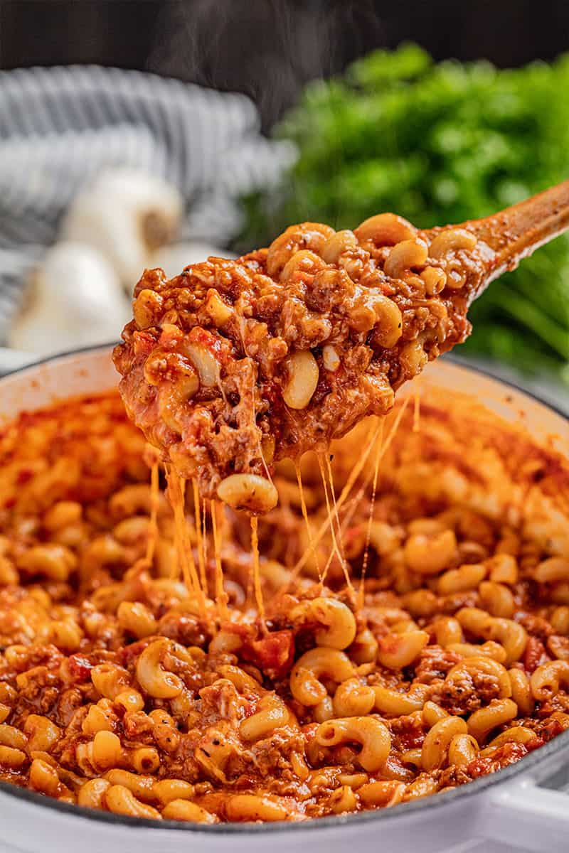 Wooden spoon filled with goulash, which is held over a soup pot.