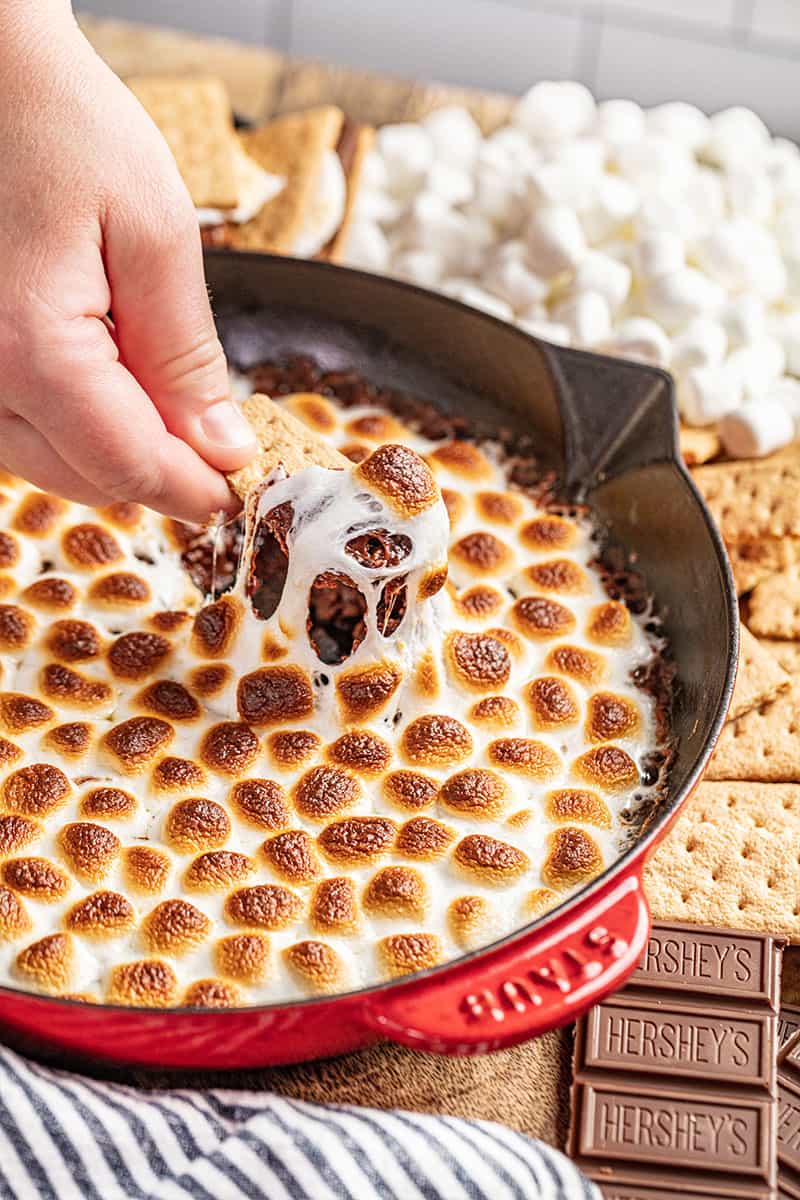 Dipping a graham cracker into a baking dish full of simple s'mores dip.
