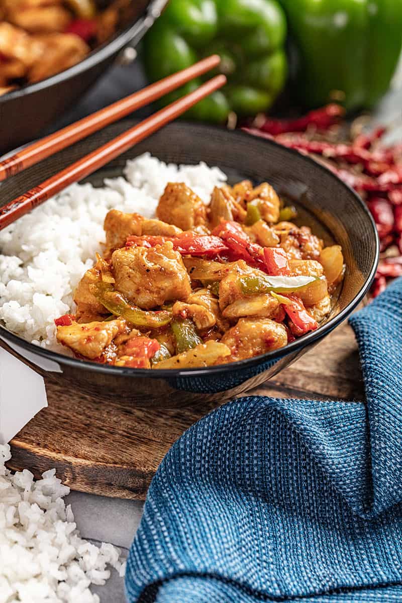 Szechuan chicken and rice in a black bowl.