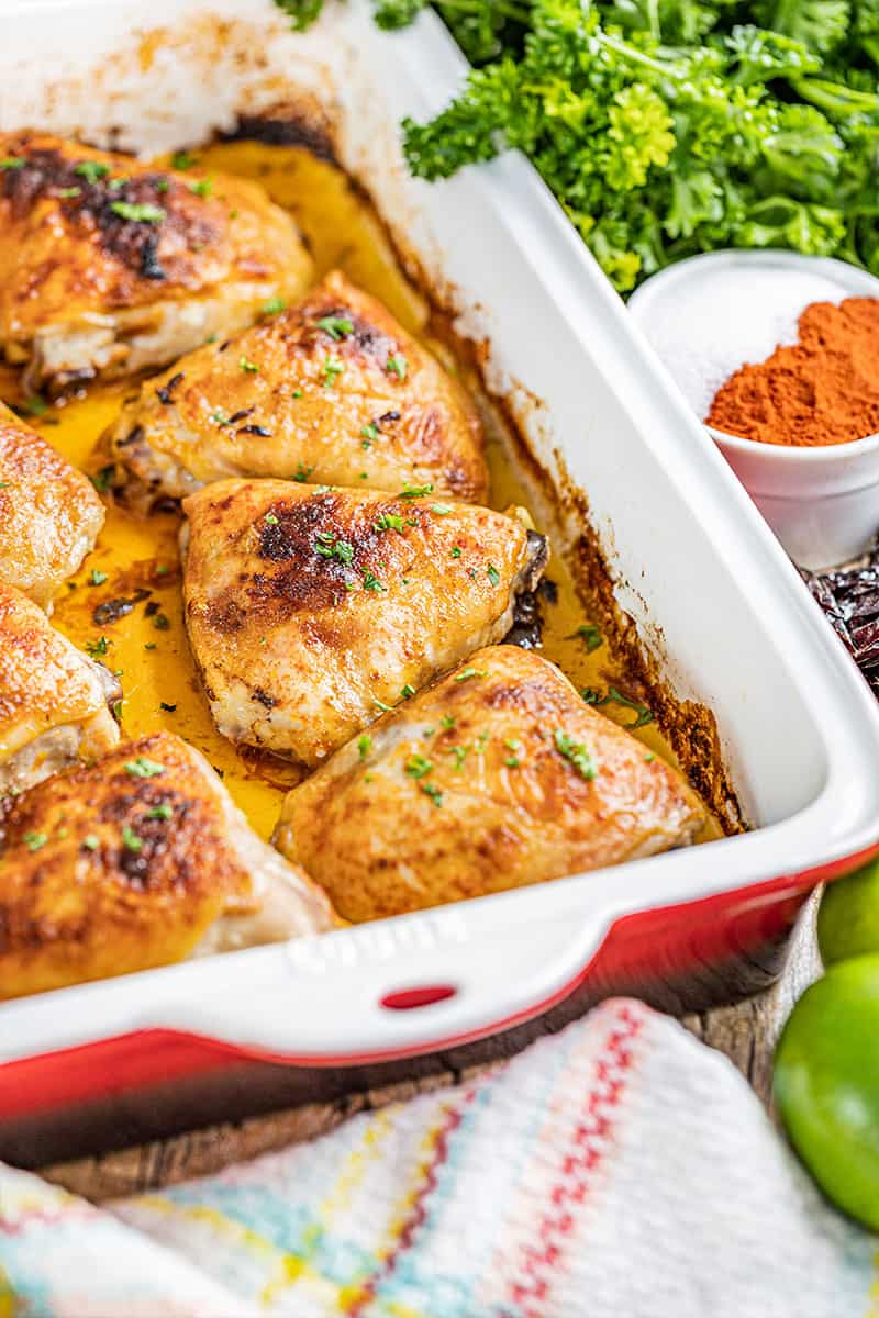 Chipotle and lime chicken thighs in a red and white baking dish.
