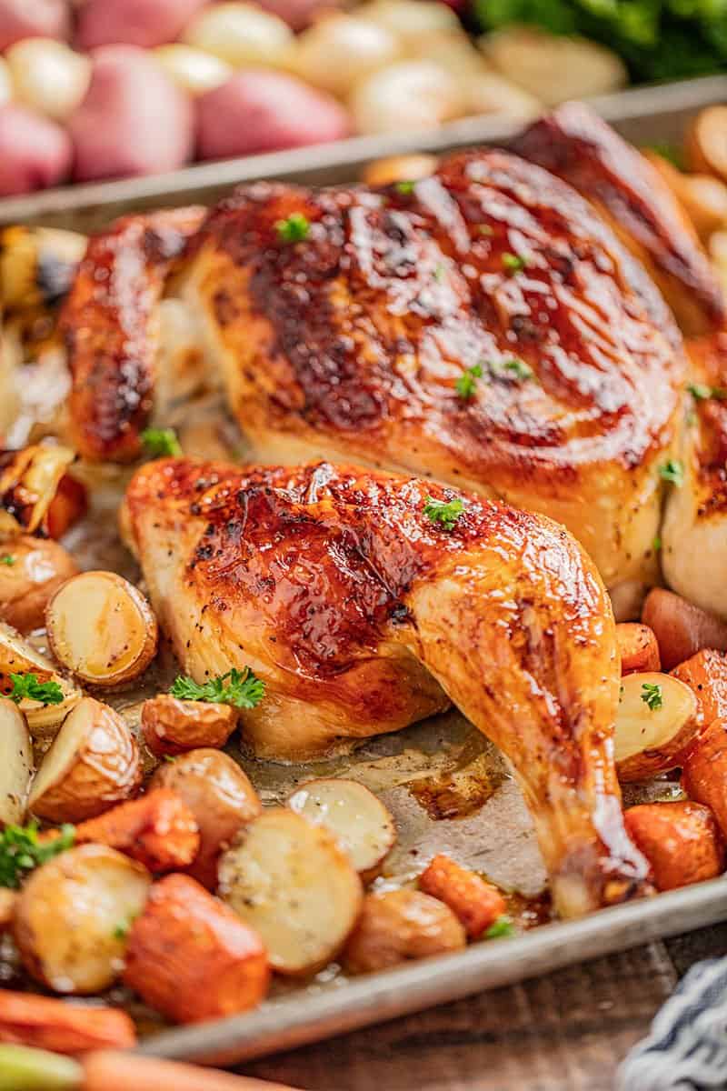 Spatchcock chicken on a baking sheet with carrots and potatoes.