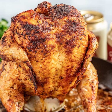 A whole roasted chicken sitting on top of a beer can in a large skillet.