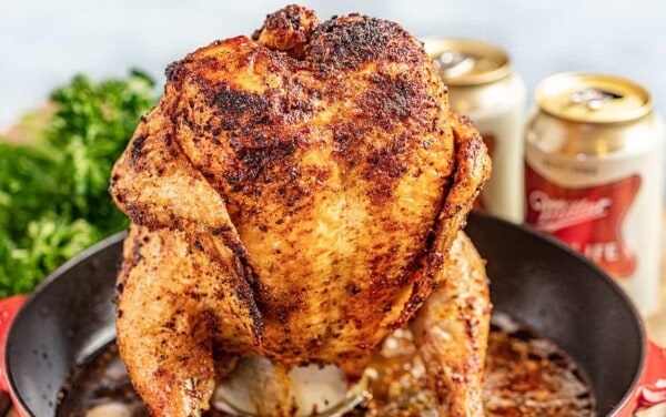 A whole roasted chicken sitting on top of a beer can in a large skillet.