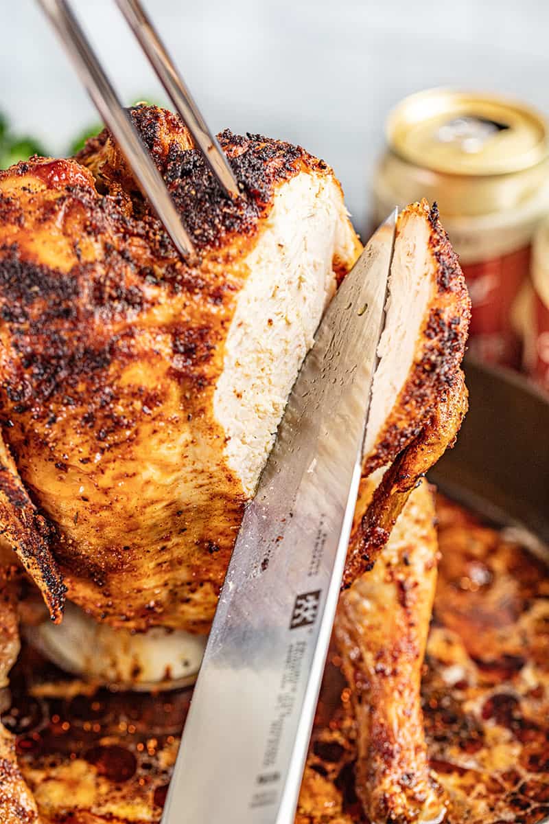 A knife slicing into a roasted whole beer can chicken.