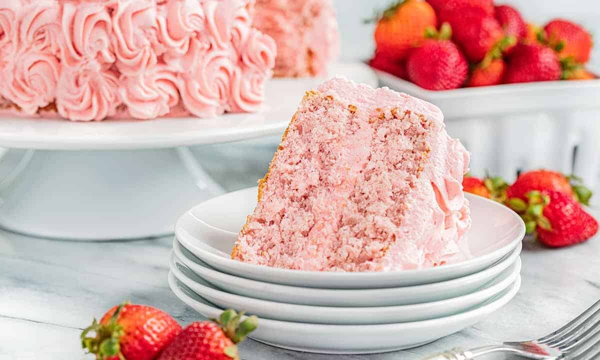 A slice of strawberry cake on a stack of dessert plates.