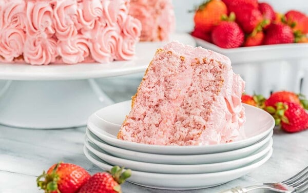 A slice of strawberry cake on a stack of dessert plates.