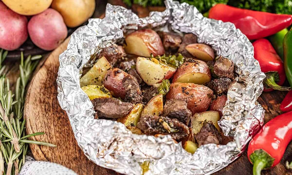 Seasoned steak and potatoes in an opened foil packet.