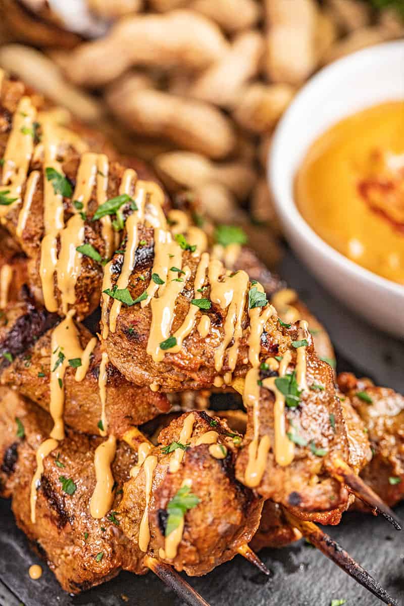 Close up view of beef satay with peanut sauce drizzled on top.