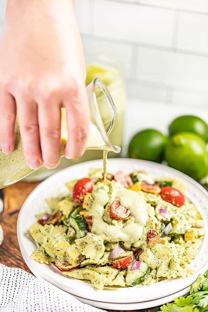 A hand pouring cilantro lime ranch dressing on top of a pasta salad.