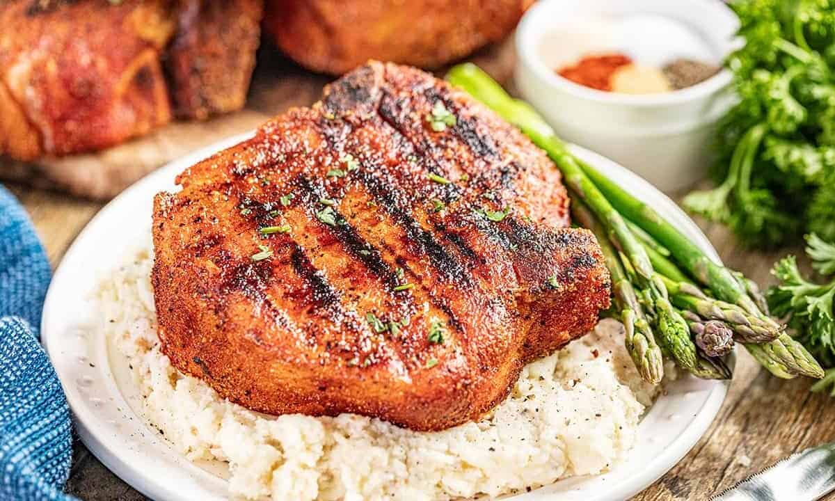 A large smoked pork chop on top of a bed of mashed potatoes on a plate.