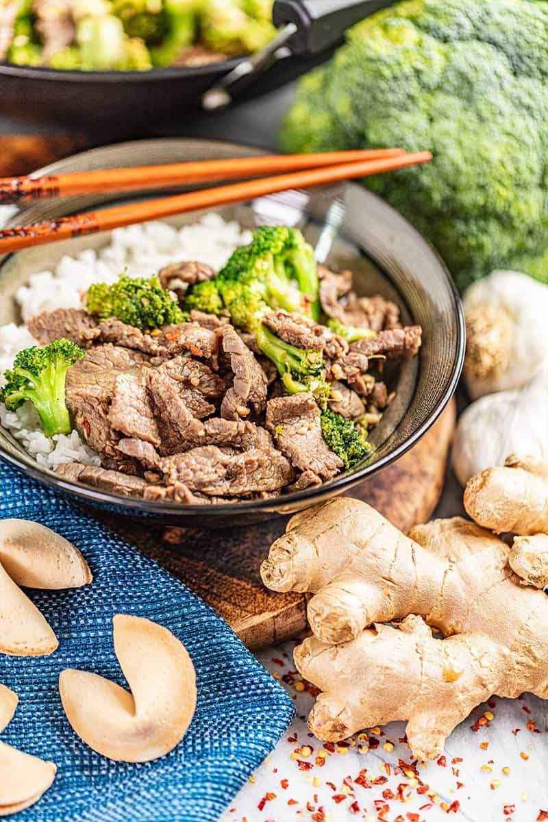 Takeout style beef and broccoli in a bowl with fresh ginger nearby.