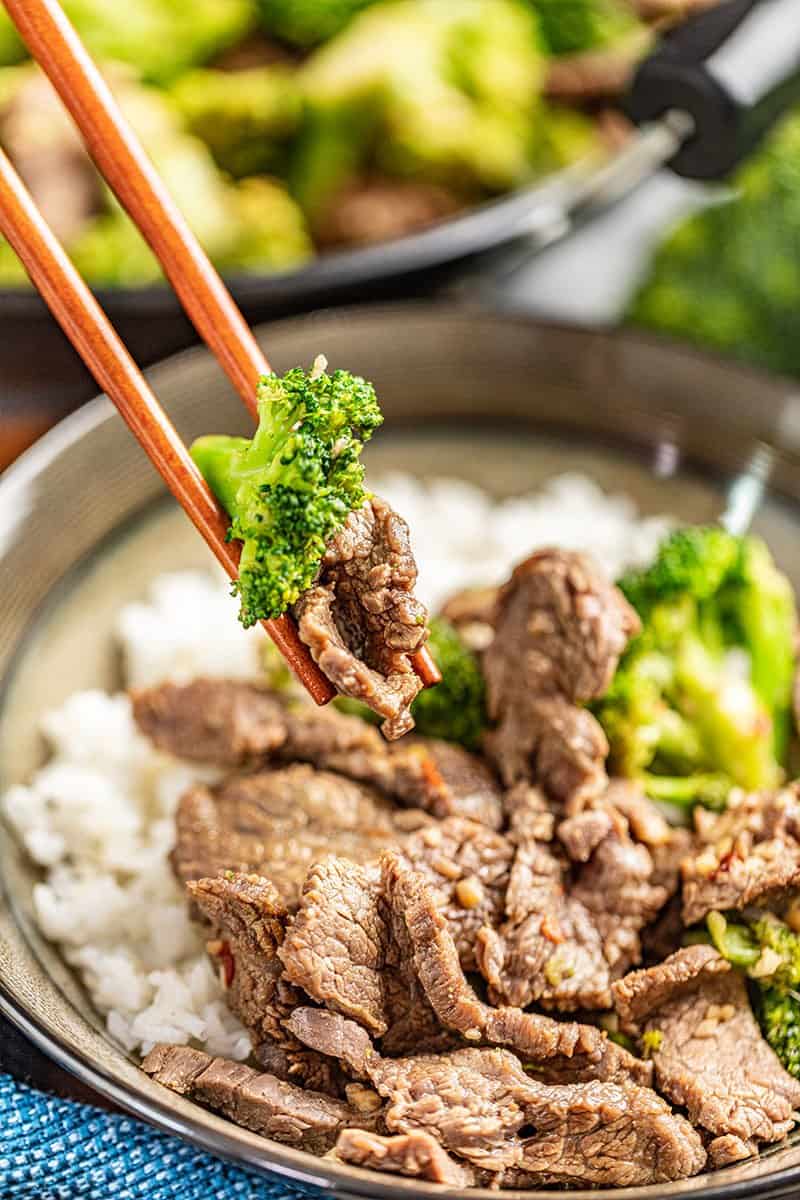 Chopsticks holding a piece of takeout style beef and broccoli.