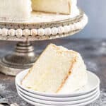 A slice removed from the most amazing white cake on a cake stand.