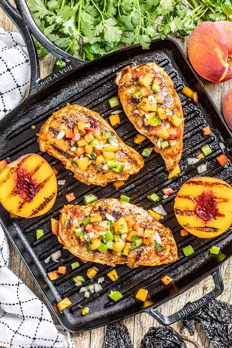 Overhead view of chipotle peach glazed grilled chicken breasts and peaches on a grill pan.