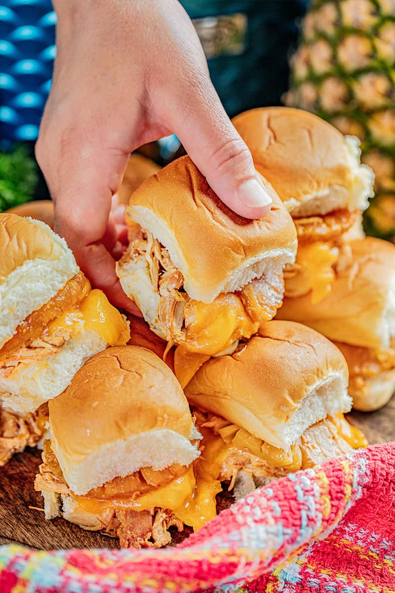 A hand picking up a cream cheese chicken slider from a stack.