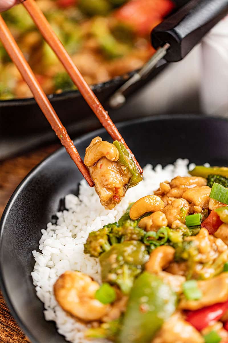 Chopsticks holding up a piece of takeout cashew chicken.