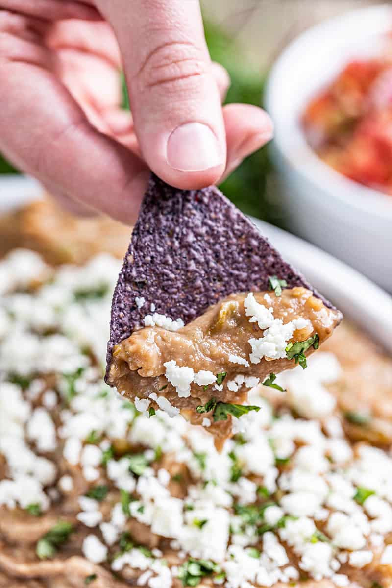 A hand holding a tortilla chip dipped in the most amazing bean dip.