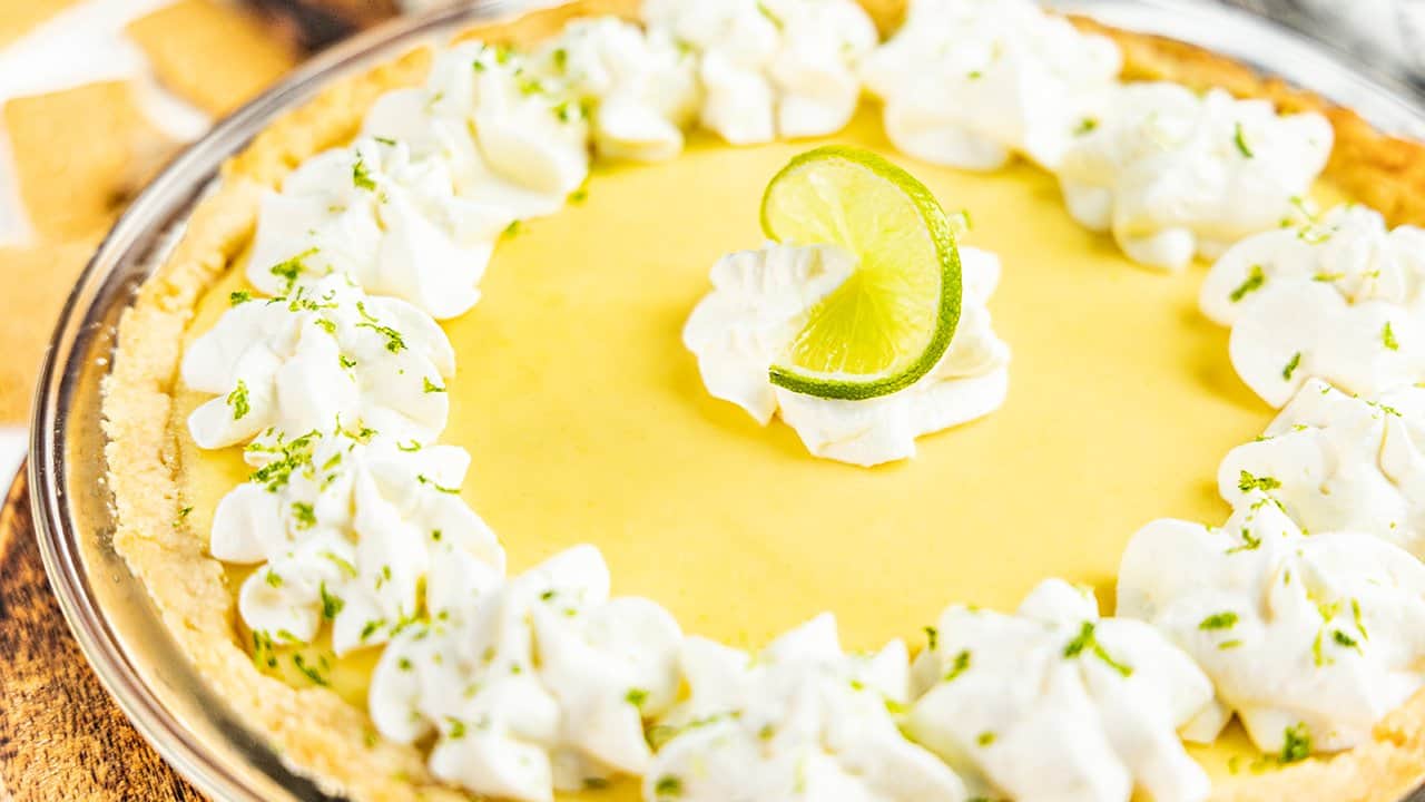 Close up view of a whole key lime pie in a glass pie plate.