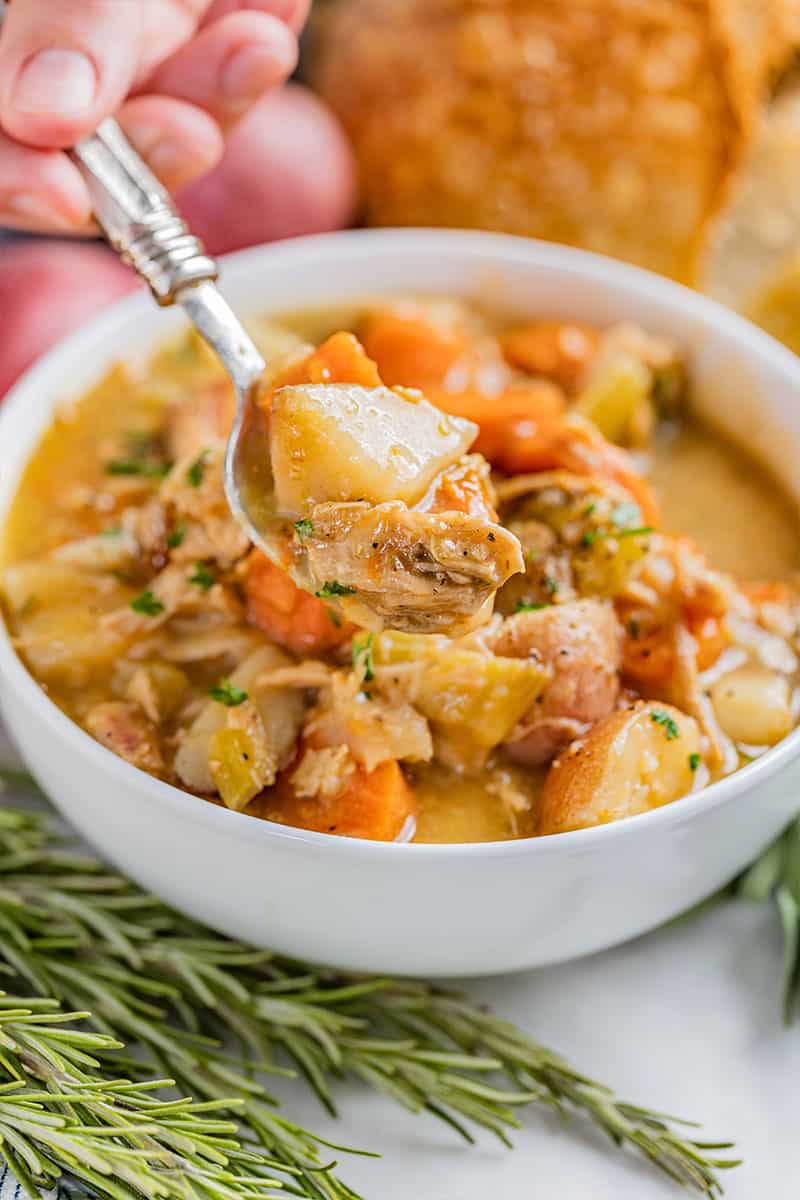 A spoon filled with old fashioned chicken stew being held over a full bowl.