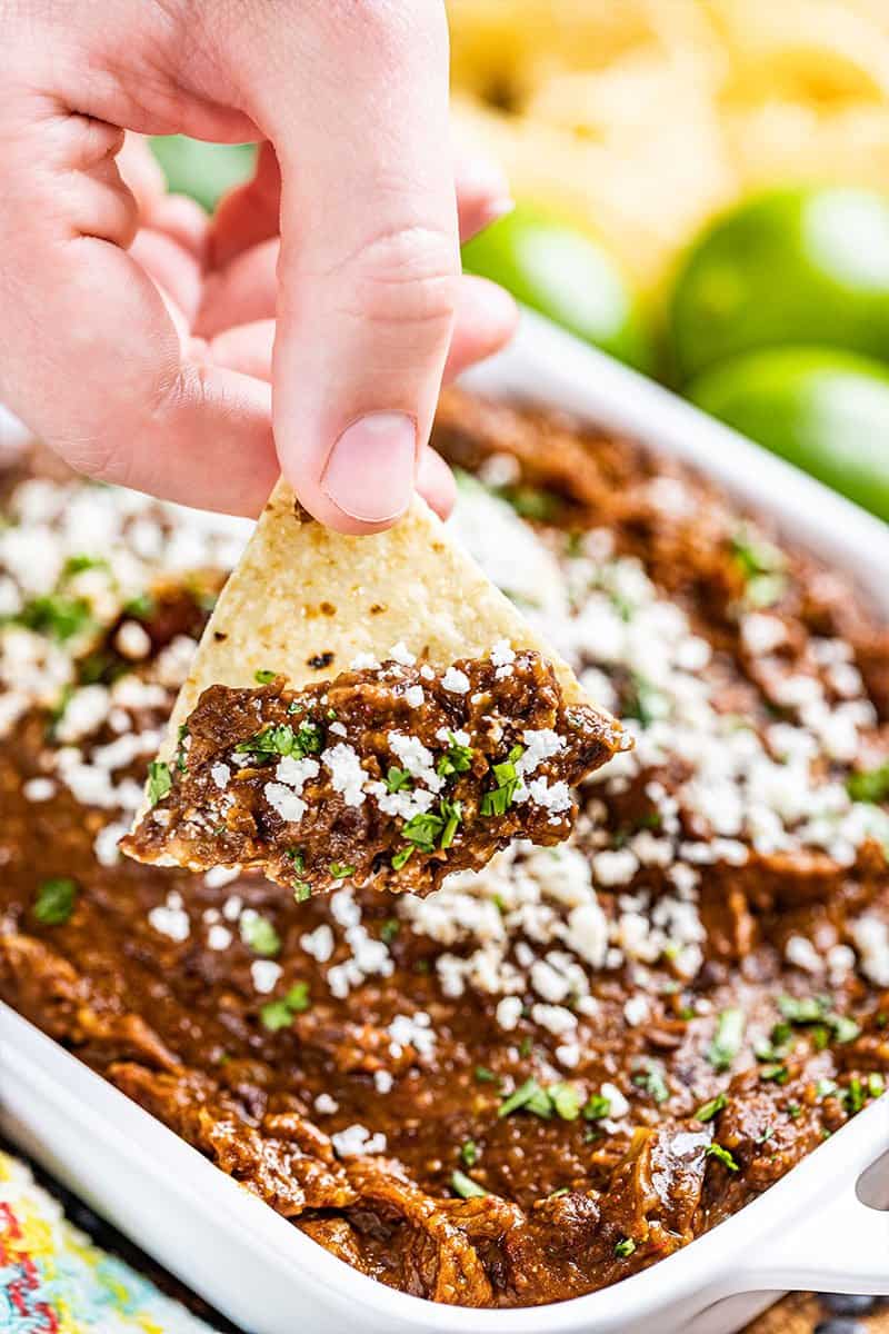 A hand holding a tortilla chip dipped in the best black bean dip.