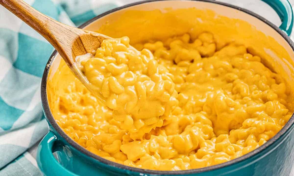 Close up view of Mac and cheese in a large pot with a wooden spoon.
