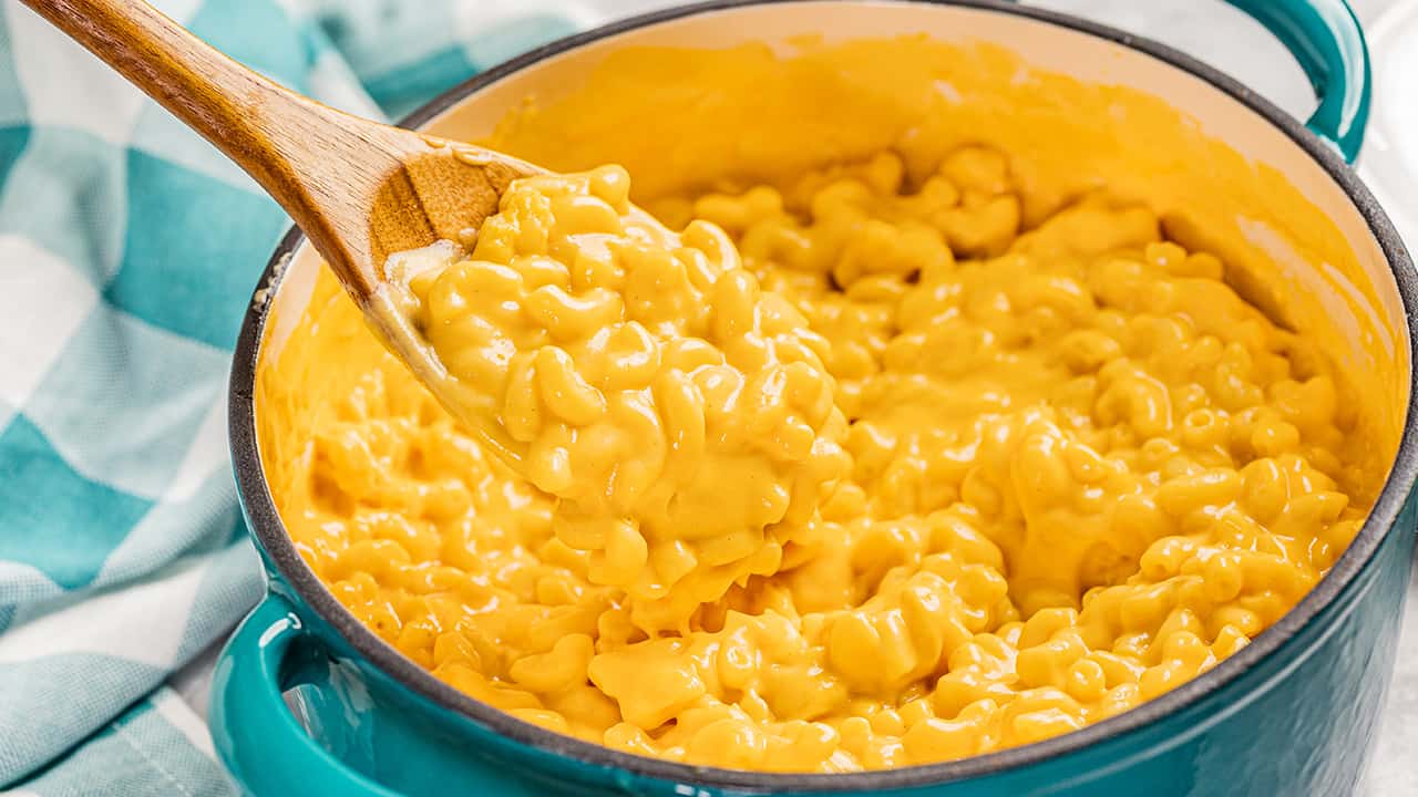 Close up view of Mac and cheese in a large pot with a wooden spoon.