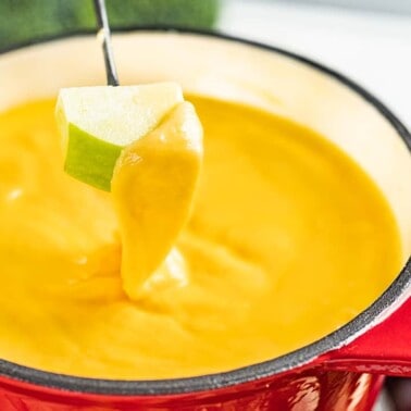 Side view of an apple piece being dipped in cheese fondue.