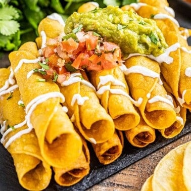 Close up view of taquitos on a black plate.