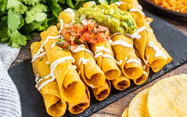 Close up view of taquitos on a black plate.