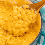 A close up view of a spoonful of creamy mac and cheese being scooped from a pot.