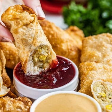 A hand dunking a thanksgiving leftover egg roll in cranberry sauce.