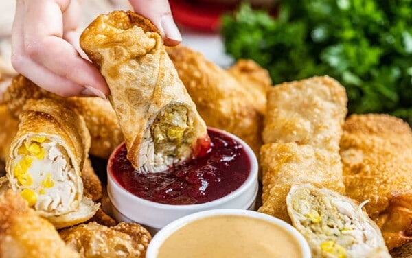 A hand dunking a thanksgiving leftover egg roll in cranberry sauce.