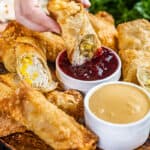 A hand dipping a Thanksgiving leftover egg roll into cranberry sauce.