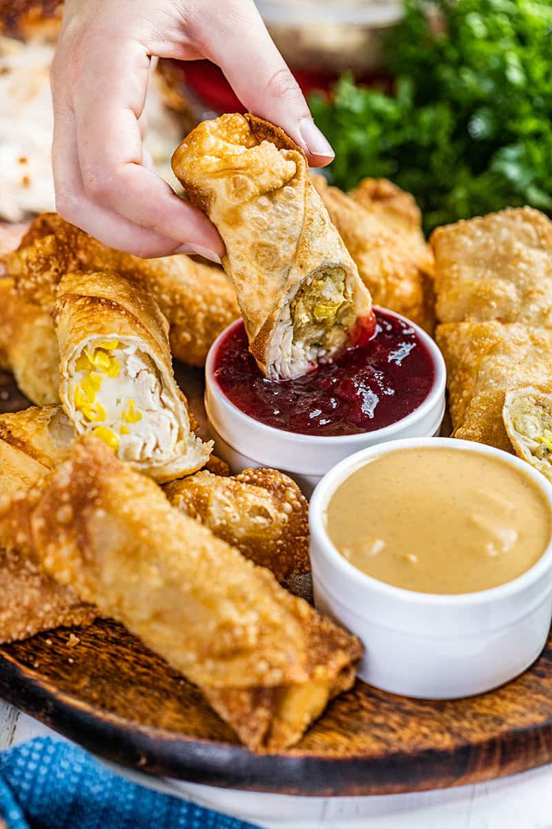 A hand dipping a Thanksgiving leftover egg roll into cranberry sauce.