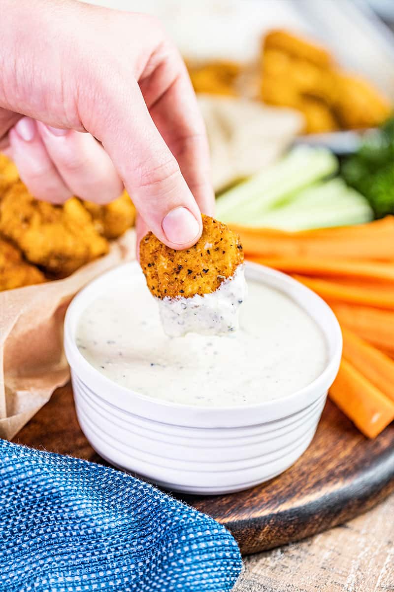 A hand holding a dipped buffalo chicken bite over a bowl of ranch.