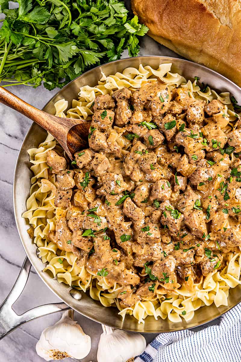 Overhead view of beef and noodles in a skillet with a wooden spoon.