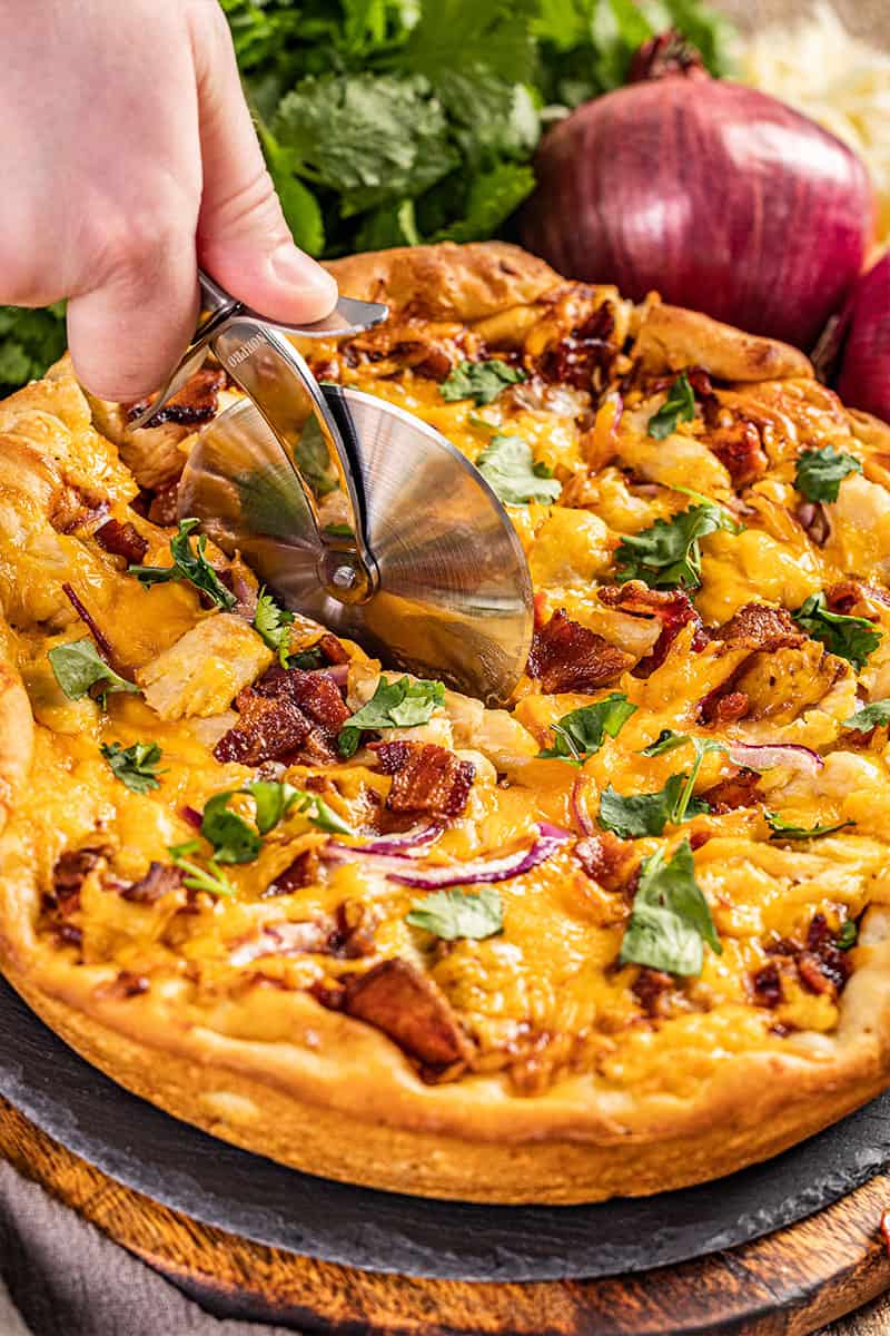 A pizza cutter slicing through a bbq chicken pizza.