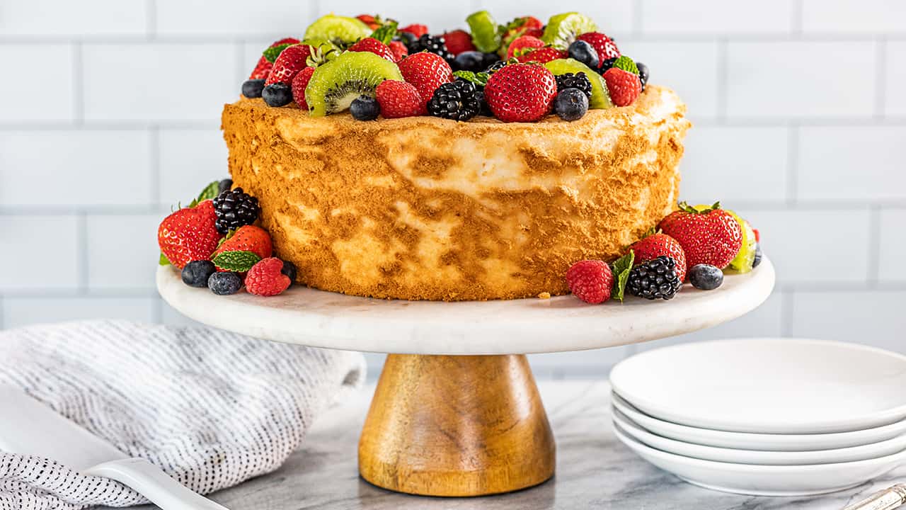 An angel food cake topped with fresh fruit sitting on a cake stand.