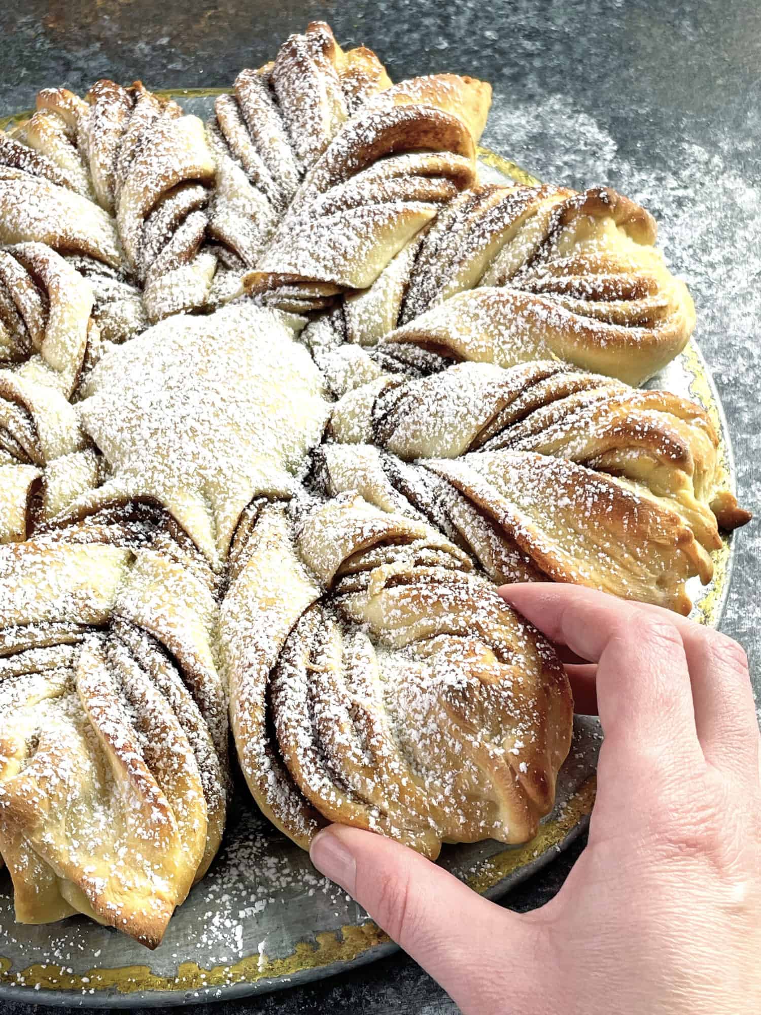 A hand taking off a piece of star bread.